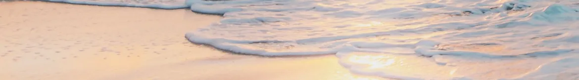 Gentle ocean waves lapping onto a sandy beach, reflecting soft golden hues from a serene sunset.