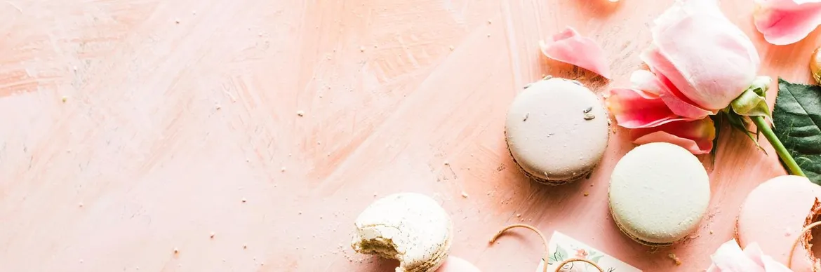 Delicate macarons, pink rose petals, and a soft pastel background create a romantic and elegant dessert setting.