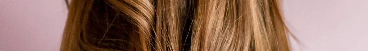 Close-up of smooth, shiny blonde hair with natural highlights, styled gracefully against a soft pink background.
