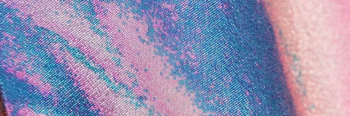 A close-up of vibrant pink and blue shimmering fabric with a textured, glittery finish, creating a mesmerising pattern.