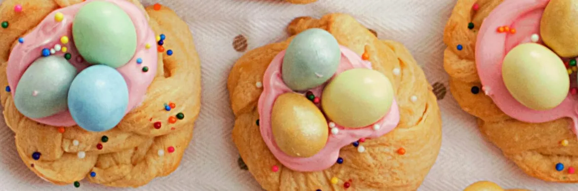 Festive Easter treats featuring braided pastries topped with pink frosting, candy eggs, and colorful sprinkles.